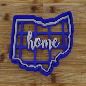 May include: Blue and white cookie cutter in the shape of the state of Ohio with the word "home" inside.