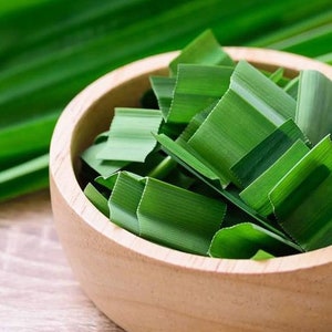 May include: A wooden bowl filled with chopped green pandan leaves. The leaves are a vibrant green color and are arranged in a neat pile.
