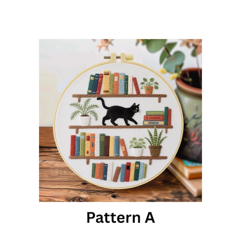 Puede incluir: Arte de aro bordado que representa un gato negro caminando sobre una estanter&iacute;a con libros coloridos y plantas en macetas. El texto "Pattern A" est&aacute; en la parte inferior de la imagen. El aro est&aacute; sobre una superficie de madera.