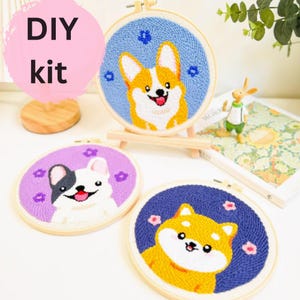 Pode incluir: Três kits de bordado DIY com diferentes raças de cães. Cada kit inclui um aro, fio e um padrão. Os cães são um corgi, um bulldogue francês e um shiba inu.