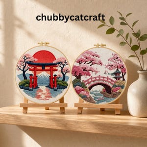 Peut inclure: Deux cerceaux brodés avec des paysages japonais. L'un présente une porte torii rouge, le Mont Fuji et un soleil levant. L'autre représente un pont, une pagode et des fleurs de cerisier. Les deux sont exposés sur des chevalets en bois.