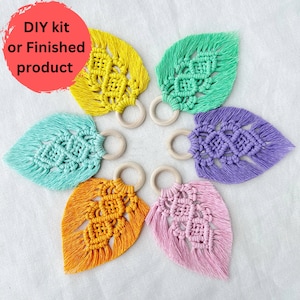 May include: Six colourful macrame leaf ornaments with wooden rings. The leaves are in shades of yellow, green, purple, blue, orange, and pink. DIY kit or finished product.