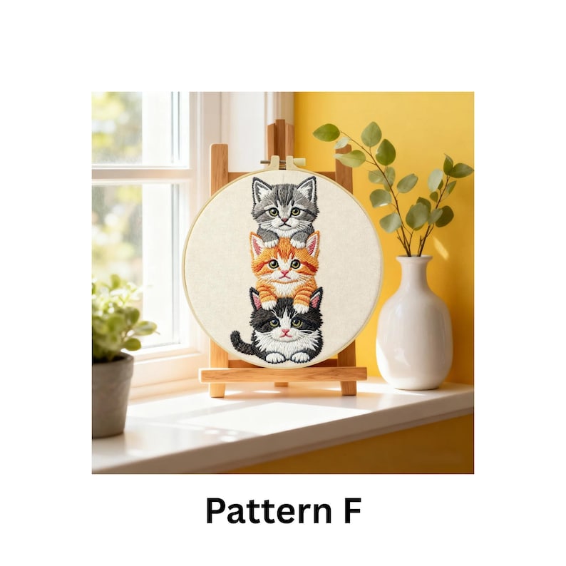 Puede incluir: Un bastidor de bordado con tres gatitos apilados en gris, naranja y blanco y negro. El bastidor se exhibe en un caballete de madera. El texto "Pattern F" est&aacute; debajo.