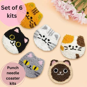 Op de afbeelding: Set van zes katvormige punch needle onderzetter kits. De onderzetters zijn in verschillende kleuren, waaronder zwart, wit, oranje, bruin en grijs, met geborduurde details. De tekst "Set of 6 kits" en "Punch needle coaster kits" is zichtbaar.