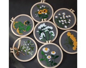 May include: Six embroidery hoops with floral designs. The hoops are made of wood and have a white background. The designs include sunflowers, daisies, and other wildflowers. The flowers are embroidered in shades of yellow, white, and green.