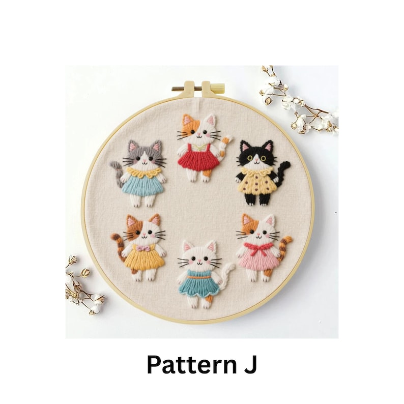 Puede incluir: Arte de aro bordado con siete figuras de gatos con vestidos coloridos. Los gatos son de varios colores, incluyendo gris, naranja y negro, sobre un fondo de tela neutra. El texto "Pattern J" est&aacute; en la parte inferior.