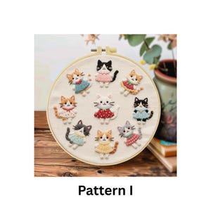Puede incluir: Un bastidor redondo con tela crema, que muestra diez dise&ntilde;os de gatos bordados. Cada gato es de un color diferente y lleva un vestido o un collar. El texto "Pattern I" est&aacute; debajo.