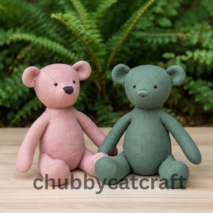 May include: Two handmade teddy bears, one pink and one green, sit side-by-side. The bears have stitched features and are made of a textured fabric. The text "chubbycatcraft" is printed in white at the bottom of the image. The background is a blurred green.
