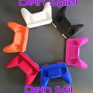 Könnte beinhalten: Eine Auswahl an farbenfrohen Gamecontroller-Griffen in Weiß, Orange, Schwarz, Pink, Rot und Blau, kreisförmig angeordnet. Der Text "Dein Spiel Dein Stil" ist in Lila oben und unten im Bild zu sehen.