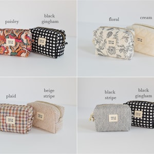 May include: A collection of small, zippered cosmetic bags in various patterns. The bags include paisley, black gingham, floral, cream, plaid, beige stripe, and black stripe designs. Each bag has a small label that reads "POPE OF COTTON".