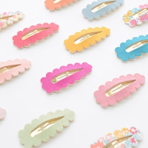 May include: Assortment of colorful hair clips with scalloped edges. The clips are made of felt and have a gold metal clasp. The colors include pink, green, blue, yellow, and orange.