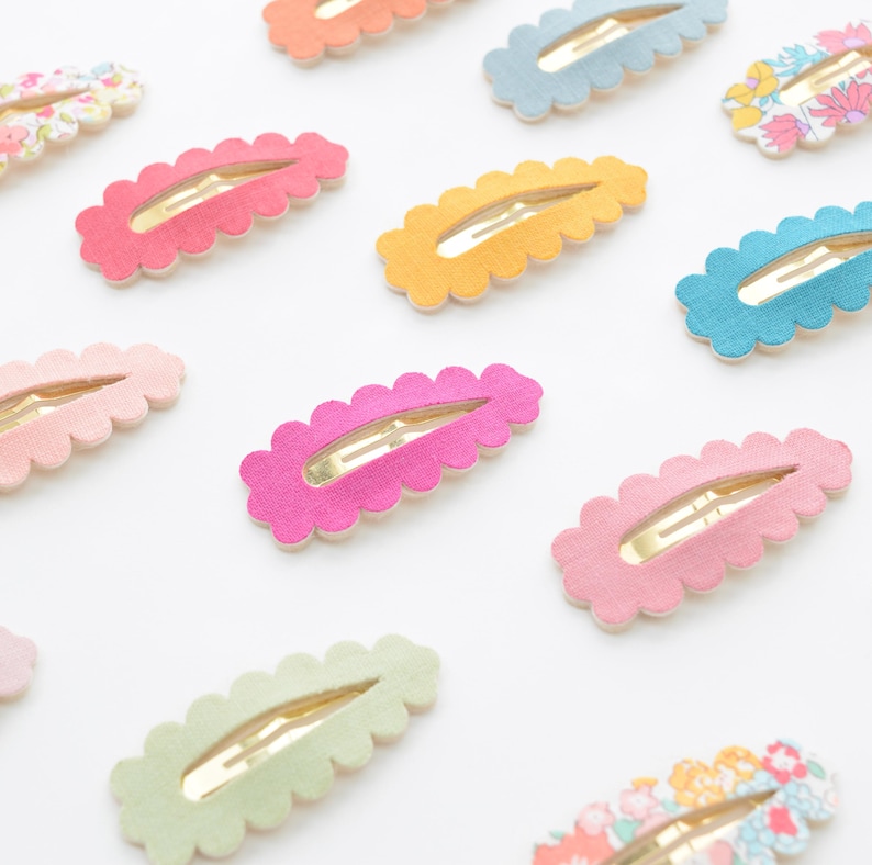 May include: Assortment of colorful hair clips with scalloped edges. The clips are made of felt and have a gold metal clasp. The colors include pink, green, blue, yellow, and orange.