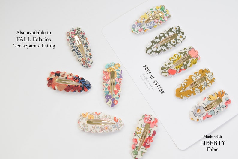 May include: A set of 9 floral patterned hair clips with gold metal clasps. The clips are arranged on a white background with the text "Pops of Cotton" and "Made with Liberty Fabric".