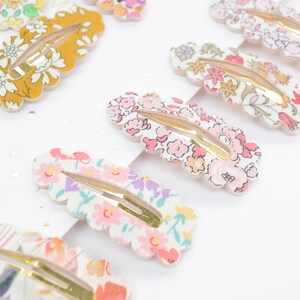 May include: A set of 10 colorful floral patterned hair clips with gold metal clasps. The clips are shaped like a scallop shell and have a white background with pink, yellow, green, and purple flowers.