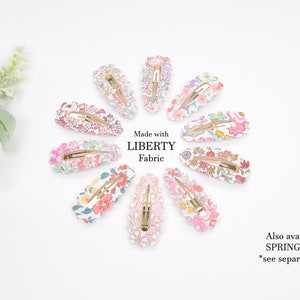 May include: A set of ten floral patterned hair clips. The clips are made with Liberty Fabric and are arranged in a circle on a white background. The text "Made with LIBERTY Fabric" is printed in the center of the circle. The text "Also available in SPRING Fabrics *see separate listing" is printed in the bottom right corner of the image.
