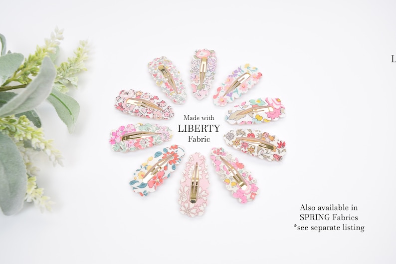 May include: A set of ten floral patterned hair clips. The clips are made with Liberty Fabric and are arranged in a circle on a white background. The text "Made with LIBERTY Fabric" is printed in the center of the circle. The text "Also available in SPRING Fabrics *see separate listing" is printed in the bottom right corner of the image.