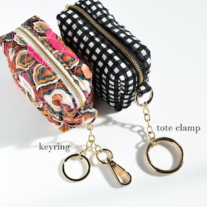 May include: Two small, rectangular pouches with gold zippers and keychains. One is patterned with a colorful floral design, the other with a black and white gingham pattern. The text "keyring" and "tote clamp" are visible.
