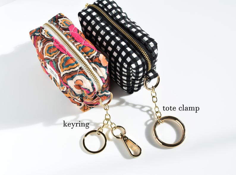 May include: Two small, rectangular pouches with gold zippers and keychains. One is patterned with a colorful floral design, the other with a black and white gingham pattern. The text "keyring" and "tote clamp" are visible.