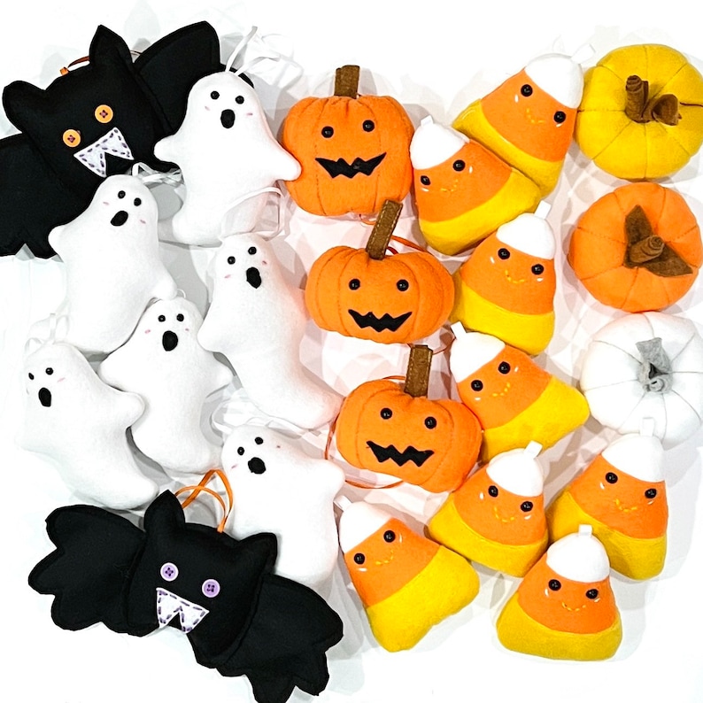 May include: A collection of Halloween-themed felt ornaments. The assortment includes black bats, white ghosts, orange pumpkins, and candy corn. The pumpkins have brown stems and carved jack-o'-lantern faces. The candy corn has smiling faces.