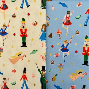 May include: Two fabric swatches with a whimsical Nutcracker theme. One is off-white, the other light blue. Both feature repeating patterns of ballerinas, nutcrackers, angels, and sweets in red, blue, green, and gold.