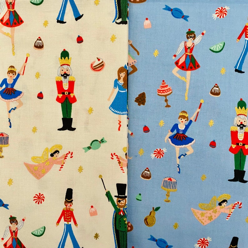 May include: Two fabric swatches with a whimsical Nutcracker theme. One is off-white, the other light blue. Both feature repeating patterns of ballerinas, nutcrackers, angels, and sweets in red, blue, green, and gold.