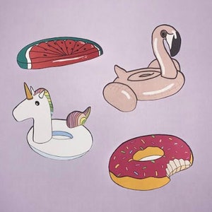 Puede incluir: Cuatro flotadores de piscina inflables: una sandía, un flamenco, un unicornio y una dona. La dona es rosa con chispas y tiene un mordisco.
