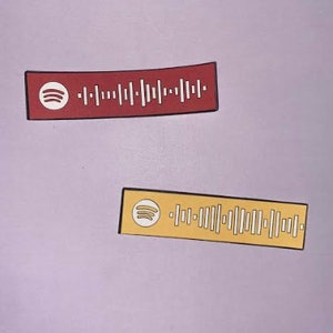 May include: Two rectangular stickers with a Spotify logo and a barcode. The top sticker is red and the bottom sticker is yellow.