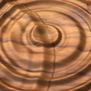 Puede incluir: Primer plano de una superficie de madera con un patr&oacute;n circular de anillos conc&eacute;ntricos, que se asemejan a las ondas en el agua. La madera tiene un color c&aacute;lido, marr&oacute;n con vetas m&aacute;s oscuras.