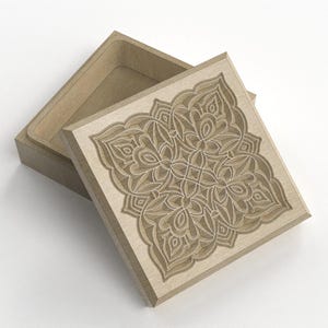 May include: A wooden box with a square lid, partially open. The lid features an intricate, symmetrical floral design carved into the wood. The box is a light brown color, and the design is a lighter shade of brown.