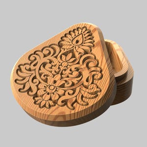 Könnte beinhalten: Eine Holzschmuckschatulle in Tropfenform mit aufwendigen Blumenschnitzereien auf dem Deckel. Die Schatulle ist geöffnet und gibt den Blick ins Innere frei. Das Holz hat eine natürliche, hellbraune Farbe.