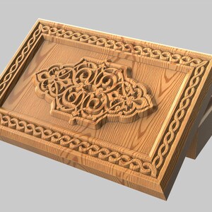 Könnte beinhalten: Dekorative Holzplatte mit einem verzierten, geschnitzten Blumendesign in der Mitte. Die Platte hat einen rechteckigen Rahmen mit einem sich wiederholenden seilartigen Muster. Das Holz hat eine hellbraune Farbe.