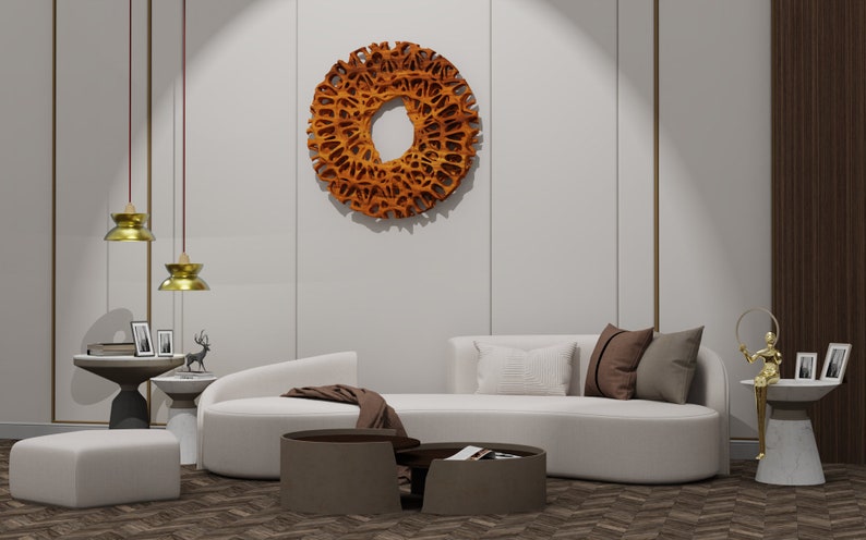 May include: A white curved sofa with brown throw pillows and a brown blanket. The sofa is in a living room with a wooden floor and a large wooden wall sculpture hanging on the wall. There are two gold pendant lights hanging from the ceiling.