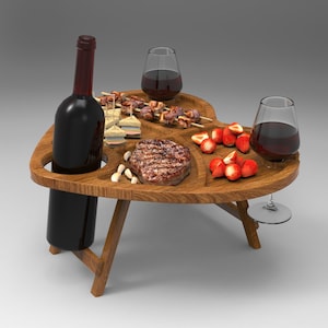 May include: A wooden heart-shaped picnic table with a bottle of wine, two glasses of wine, a steak, skewers of food, and strawberries.