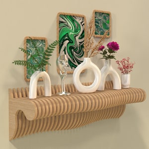 Könnte beinhalten: Ein Wandregal aus Holz mit geschwungenem Design, mit weißen Keramikvasen mit Trockenblumen und einer Glasvase mit einer silbernen Skulptur. Das Regal ist mit drei gerahmten abstrakten Gemälden mit grünen und weißen Wirbeln verziert.