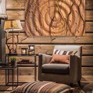 May include: A brown leather armchair with a striped throw pillow and a brown throw pillow sits in a room with wood paneling and a large abstract painting on the wall.
