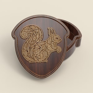 May include: A wooden acorn-shaped box with a detailed, intricate squirrel design carved into the lid. The squirrel is made of gold-coloured wood and is surrounded by a brown wooden frame.