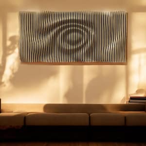 May include: A white, wooden wall sculpture with a wavy, circular pattern. The sculpture is hanging on a beige wall above a brown couch.