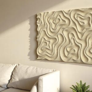 May include: A rectangular, beige wall art piece with a textured, swirling pattern hangs on a light beige wall. The artwork's design resembles flowing waves or topographical lines. A white sofa and green plant are in the foreground.