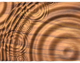 Puede incluir: Primer plano de una superficie de madera con un patrón de círculos concéntricos, que se asemejan a las ondas en el agua. La madera tiene un color cálido, marrón con un sutil patrón de veta.