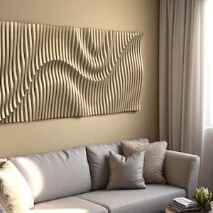 May include: A large, rectangular wooden wall art piece with a wave-like design. The artwork is made of vertical wooden slats that curve and undulate, creating a three-dimensional effect. The piece is mounted on a beige wall above a gray sofa.