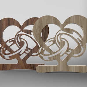 Peut inclure: Deux supports de bague en bois en forme de cœur avec des découpes complexes d'anneaux entrelacés. Les supports sont en bois brun de différentes nuances.