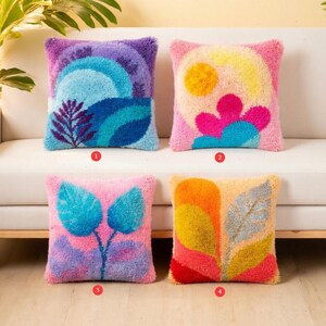 Peut inclure: Quatre coussins carrés décoratifs avec des motifs abstraits colorés. Les coussins présentent une variété de motifs, notamment un coucher de soleil, des fleurs et des feuilles. Les coussins sont en matière texturée et sont exposés sur un canapé blanc.