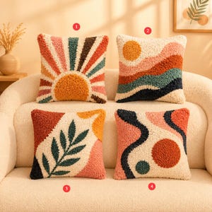 Könnte beinhalten: Vier quadratische Kissen mit strukturierten, getufteten Designs. Die Kissen weisen abstrakte und geometrische Muster auf, darunter ein Sonnenaufgang, eine Landschaft mit Sonne, ein Blatt und ein wellenförmiges Design mit Kreisen. Die Farbpalette umfasst Orange, Rosa, Grün und Braun.