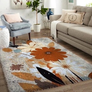 Könnte beinhalten: Ein rechteckiger Teppich mit floralem Design. Der Teppich zeigt große orangefarbene und weiße Blumen mit braunen und schwarzen Akzenten auf grauem Hintergrund. Der Teppich befindet sich in einem Wohnzimmer.