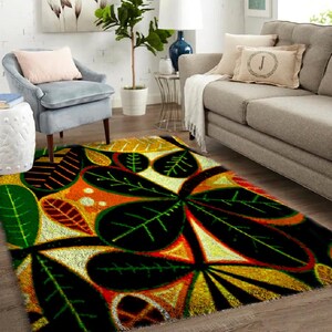 Könnte beinhalten: Ein farbenfroher Teppich mit einem botanischen Design. Der Teppich zeigt große, stilisierte Blätter in Schwarz, Grün, Orange und Gelb. Der Teppich befindet sich in einem Wohnzimmer mit Sofa, Stuhl und Beistelltisch.