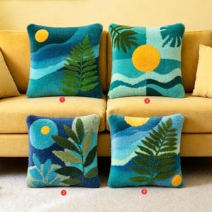 May include: Four square throw pillows with nature-themed designs. Each pillow features a different landscape with a yellow sun or moon, blue water, and green foliage. The pillows are on a yellow sofa.