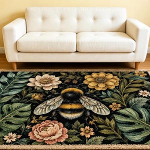 May include: A rectangular area rug featuring a black background with a large central bumblebee surrounded by detailed illustrations of green monstera leaves, ferns, and various flowers in shades of yellow, cream, and soft pink with a tan border.