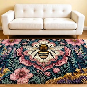 May include: A rectangular area rug featuring a central honeybee illustration surrounded by a detailed floral mandala pattern in shades of pink, teal, and yellow, with dark green foliage accents and fringed edges on the short sides of the rug.