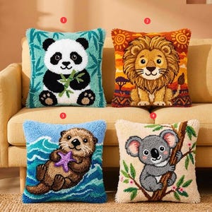 Könnte beinhalten: Vier dekorative Kissen mit Tierdesigns. Ein Panda mit Bambus, ein Löwe mit Sonnenuntergang, ein Otter mit Seestern und ein Koala auf einem Ast. Jedes Kissen hat eine strukturierte, gestickte Optik.