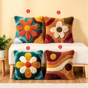 Könnte beinhalten: Vier dekorative Zierkissen mit farbenfrohen Blumenmustern. Jedes quadratische Kissen hat ein anderes Muster, darunter große Blumen und abstrakte Formen in Orange-, Gelb-, Grün- und Brauntönen. Die Kissen sind auf einer weißen Bank platziert.